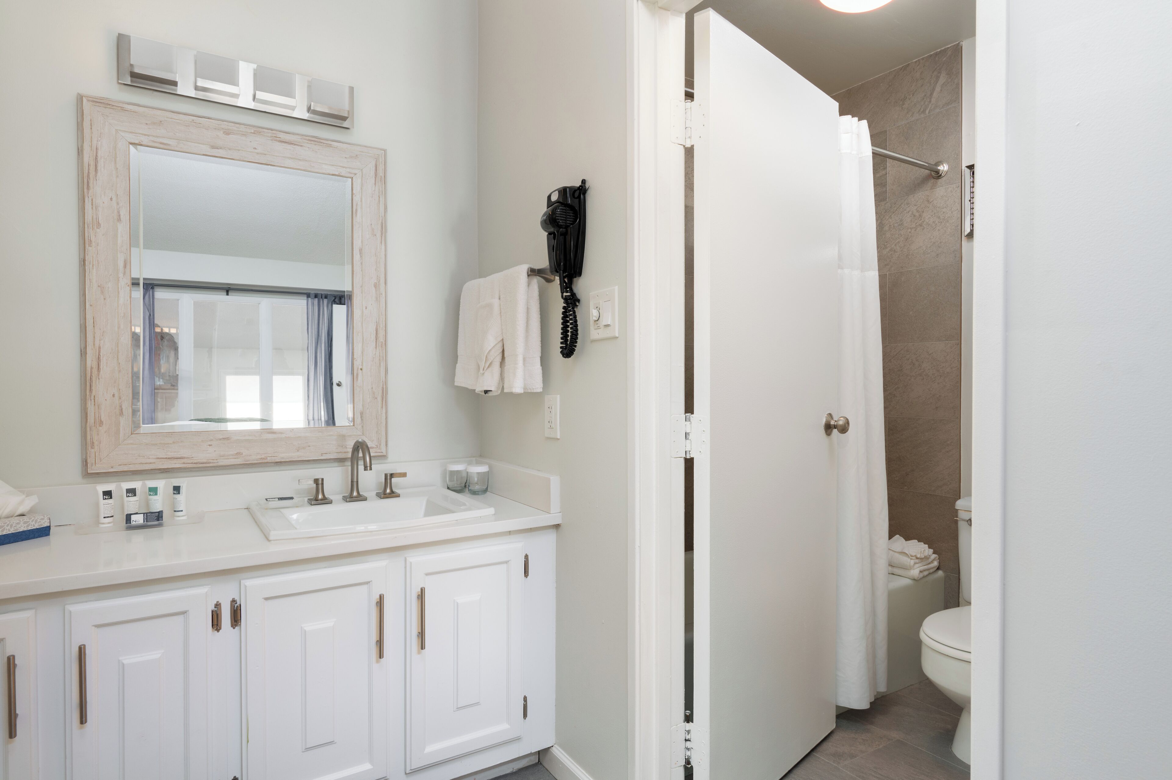A bathroom with a white sink, mirror, and toilet. There is a hairdryer on the wall and a shower curtain.