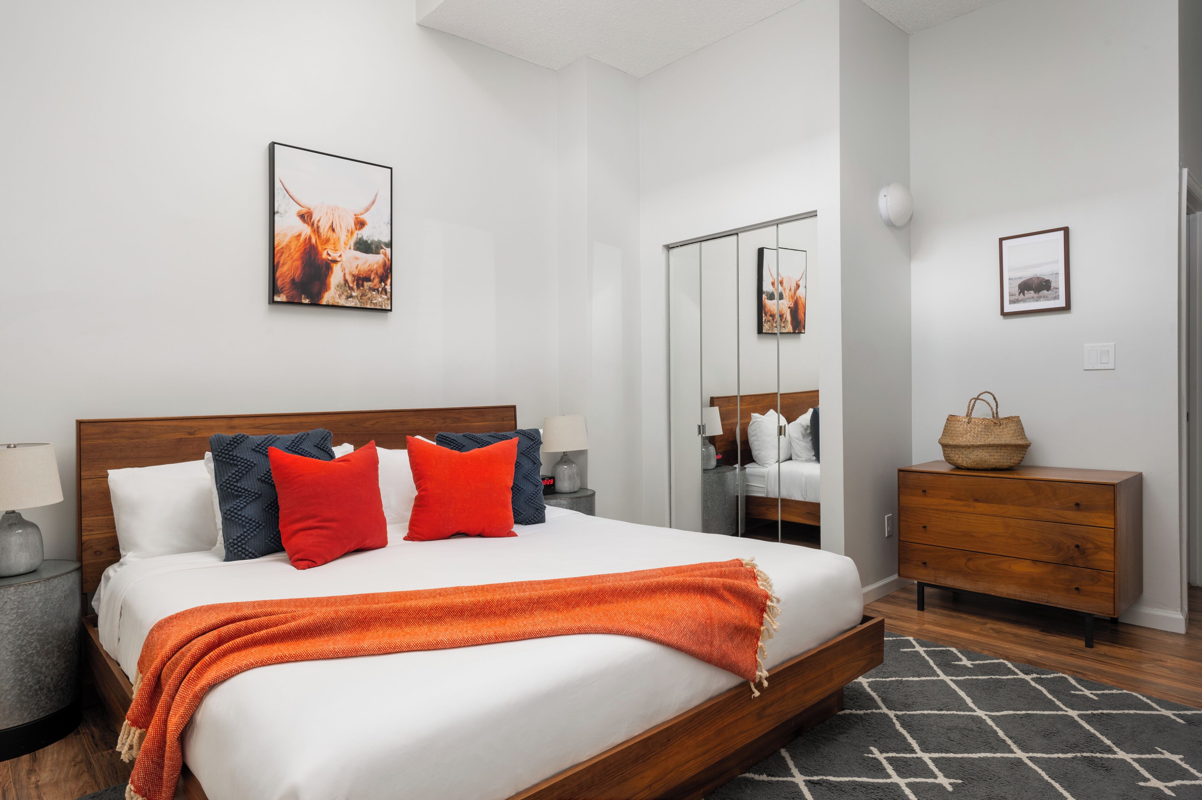 Una habitación de hotel moderna con una cama grande, un aparador de madera, un espejo y obras de arte en las paredes.