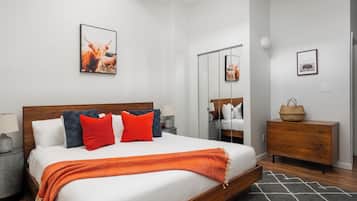 Una habitación de hotel moderna con una cama grande, un aparador de madera, un espejo y obras de arte en las paredes.