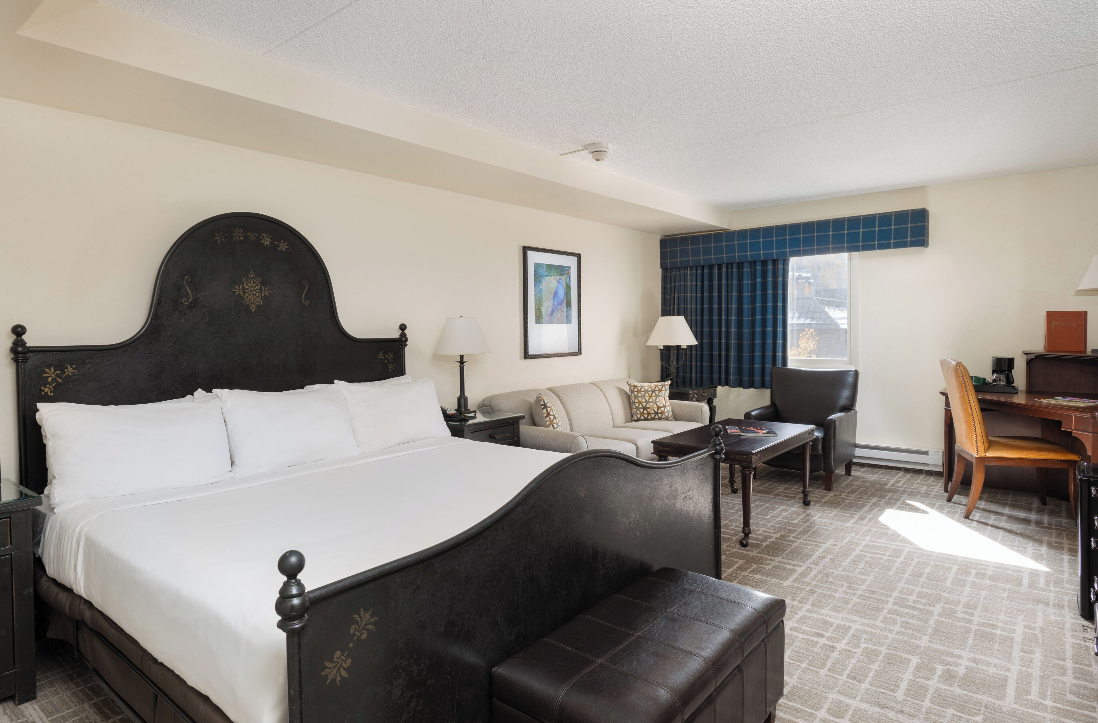 A hotel room with a large bed, a sofa, a desk, and a chair.