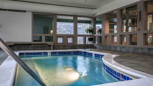 Una piscina con borde de azulejos, una escalera de metal y vistas a través de grandes ventanales.