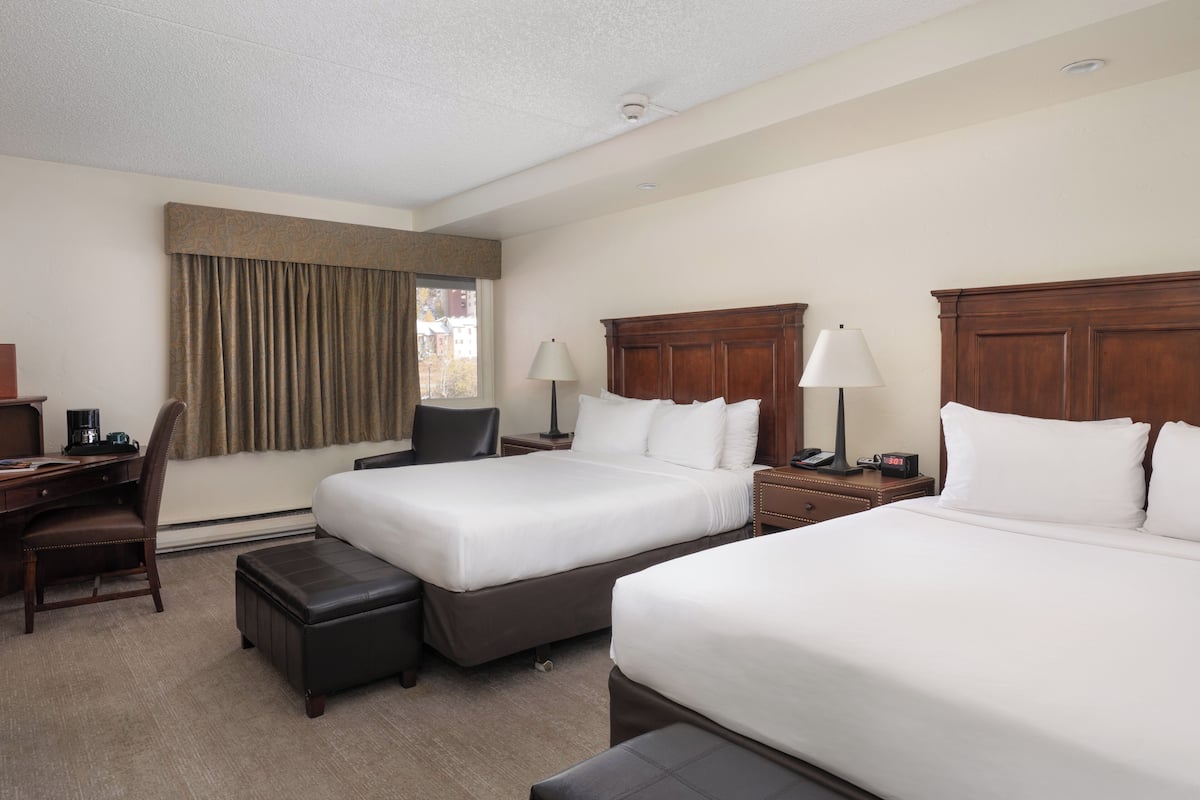 Una habitación de hotel con dos camas, un escritorio, una silla y una ventana con cortinas.