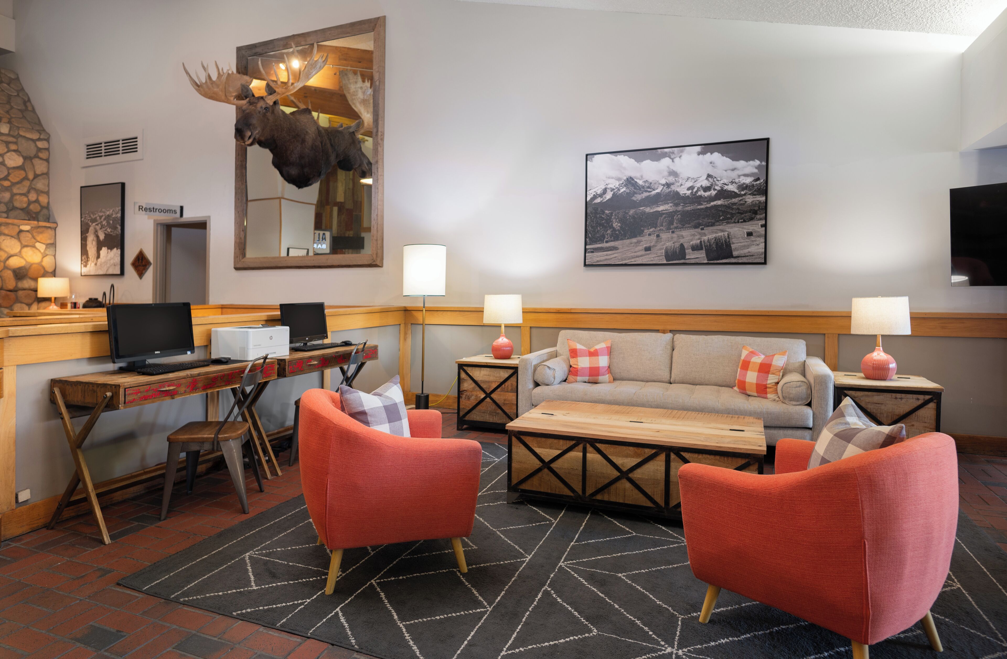 A cozy hotel lobby with a fireplace, a mounted moose head, a sofa, and a television.