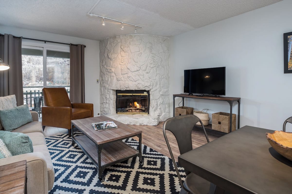 Una sala de estar acogedora con chimenea de piedra, un televisor sobre un mueble de madera y una alfombra estampada.