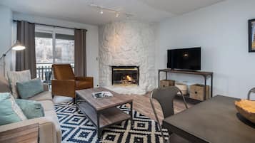 Un salon chaleureux avec une cheminée en pierre, un téléviseur posé sur un meuble en bois et un tapis à motifs.