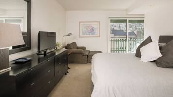 A bedroom with a bed, dresser, TV, and a window with a view of a balcony.