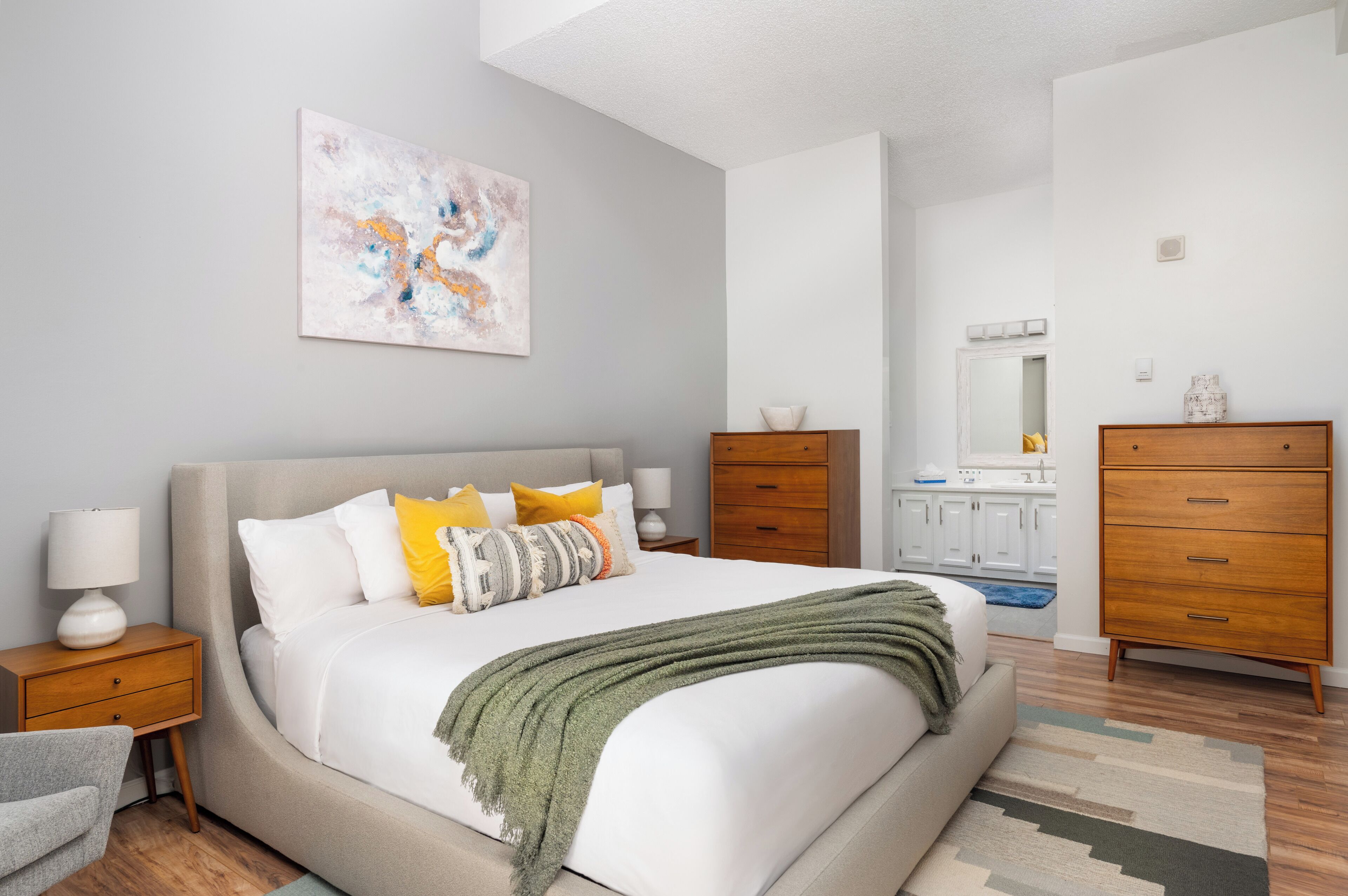 Een moderne slaapkamer met een groot bed, houten nachtkastjes, een dressoir en een zichtbare badkamer op de achtergrond.