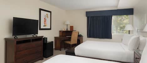 Une chambre d’hôtel avec deux lits, un bureau avec une chaise, une télévision et une fenêtre avec des rideaux.