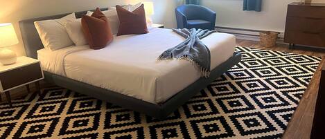 Una habitación de hotel con una cama, una silla, un aparador y una ventana con cortinas.
