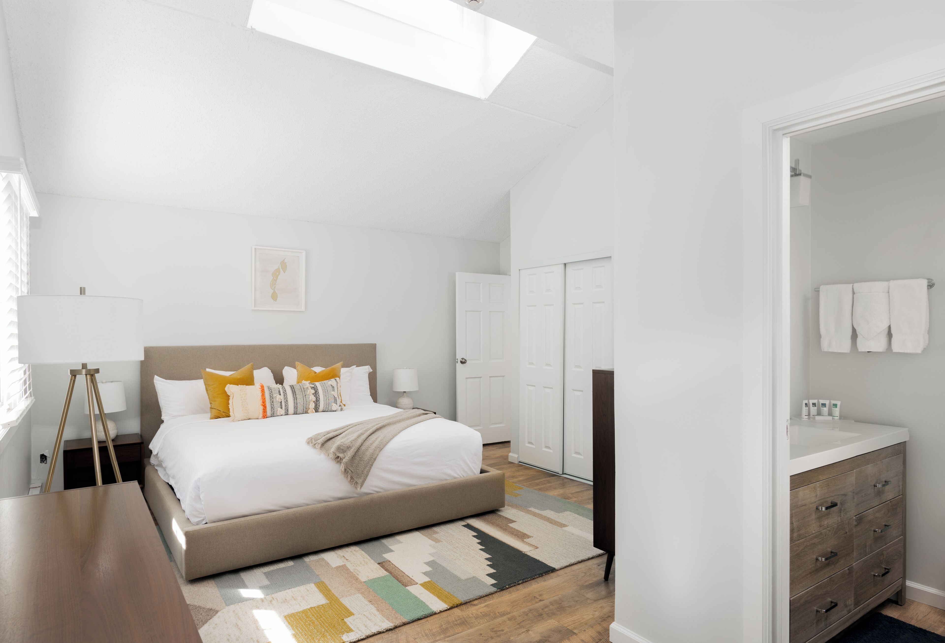 A bedroom with a large bed, a bedside table, a desk, and a wardrobe.