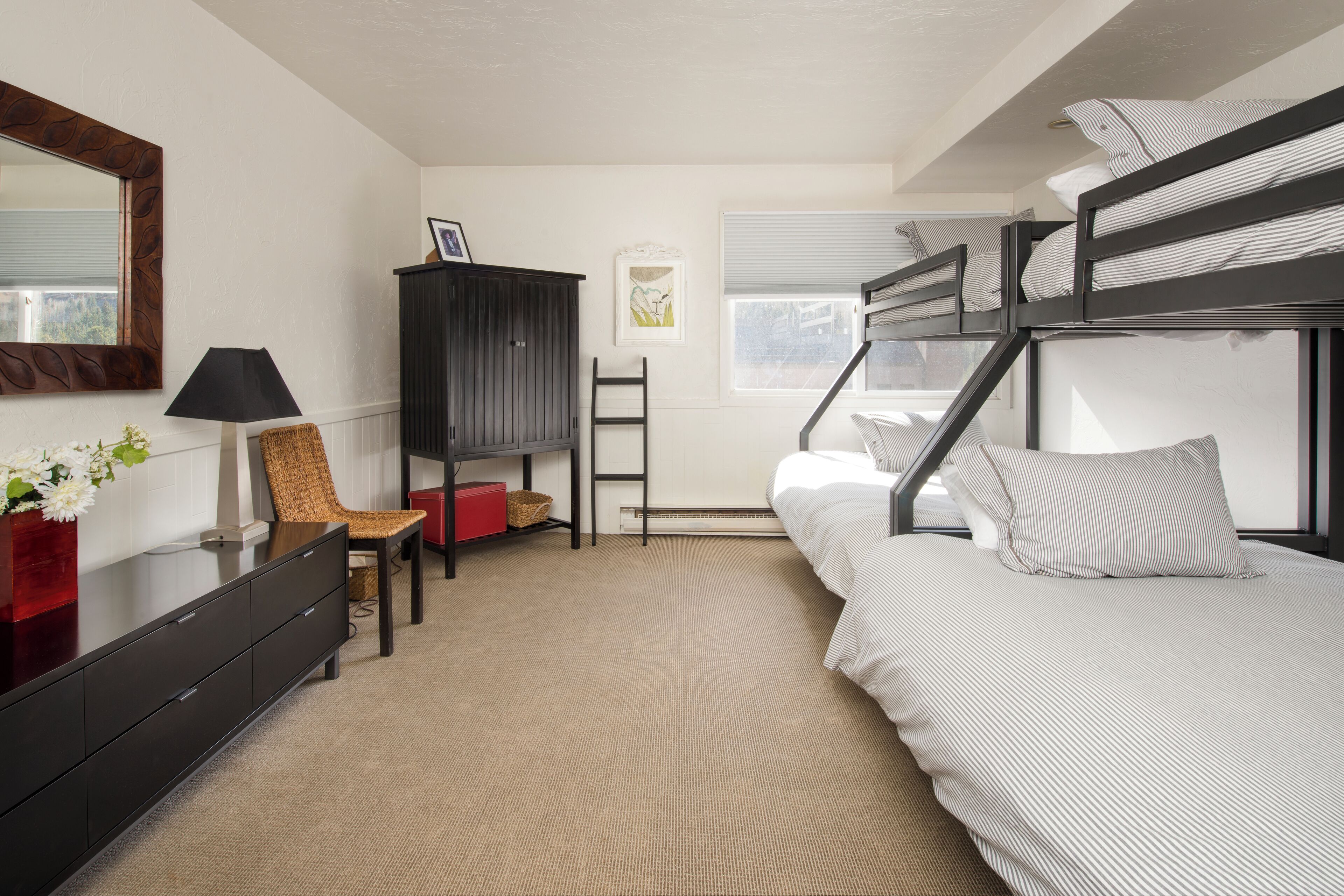 Een slaapkamer met stapelbedden, een dressoir, een stoel, een lamp en een raam met zonwering.