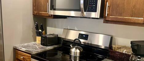 Una cucina con mobili in legno, un forno a microonde in acciaio inox, un piano cottura a gas e una macchina per il caffè.