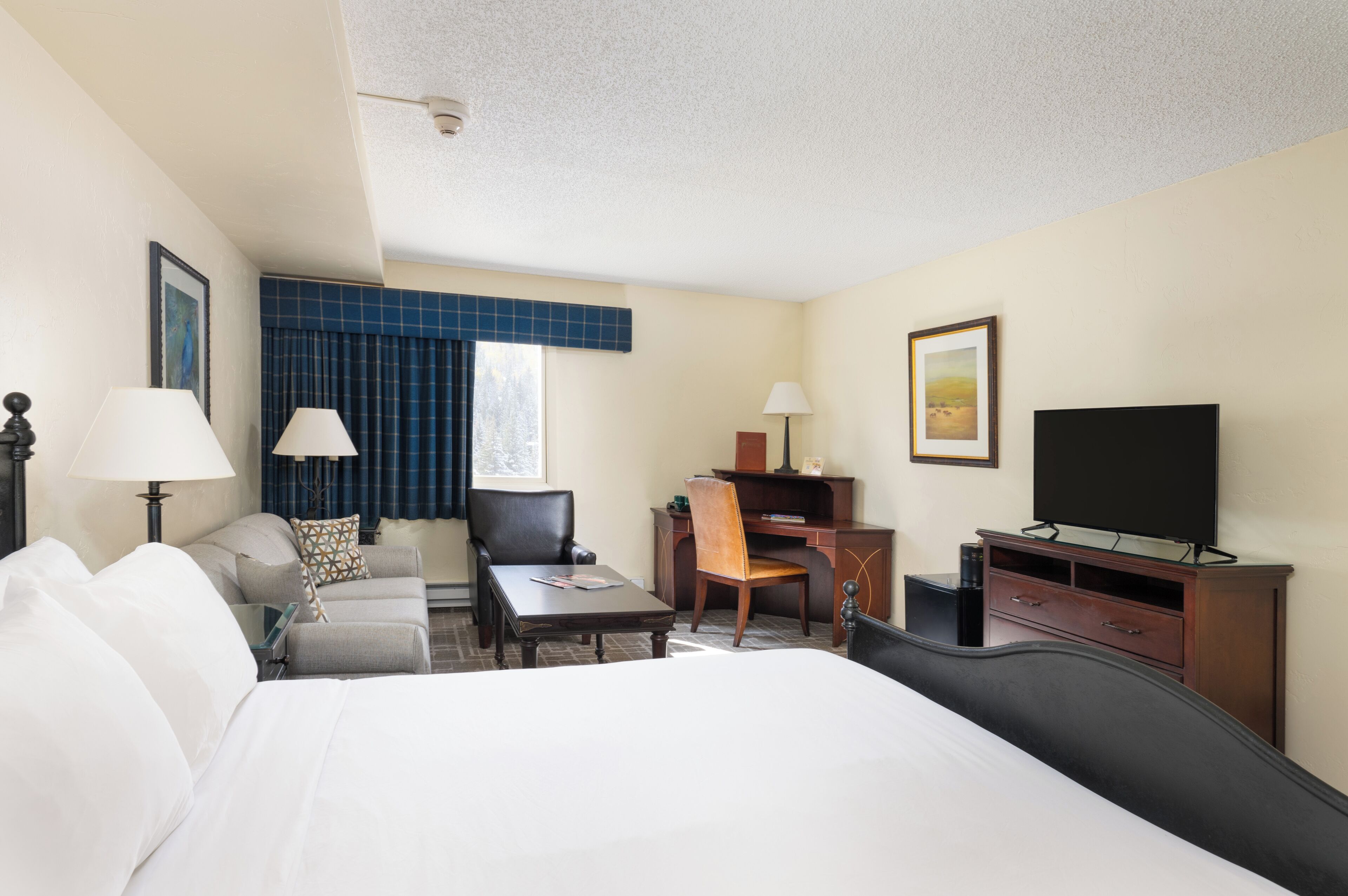 A hotel room with a bed, a desk, a chair, a television, and a window with curtains.