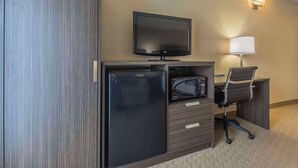 Habitación de hotel compacta con televisión de pantalla plana, refrigerador pequeño, microondas, escritorio con silla y lámpara de pared.