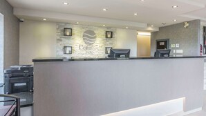 Zona de recepción de hotel con pared de piedra, mostrador de recepción y cámara de seguridad.