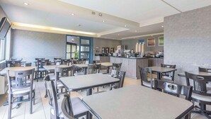 Un restaurante moderno con varias mesas y sillas, una zona de cocina y vistas a la calle.