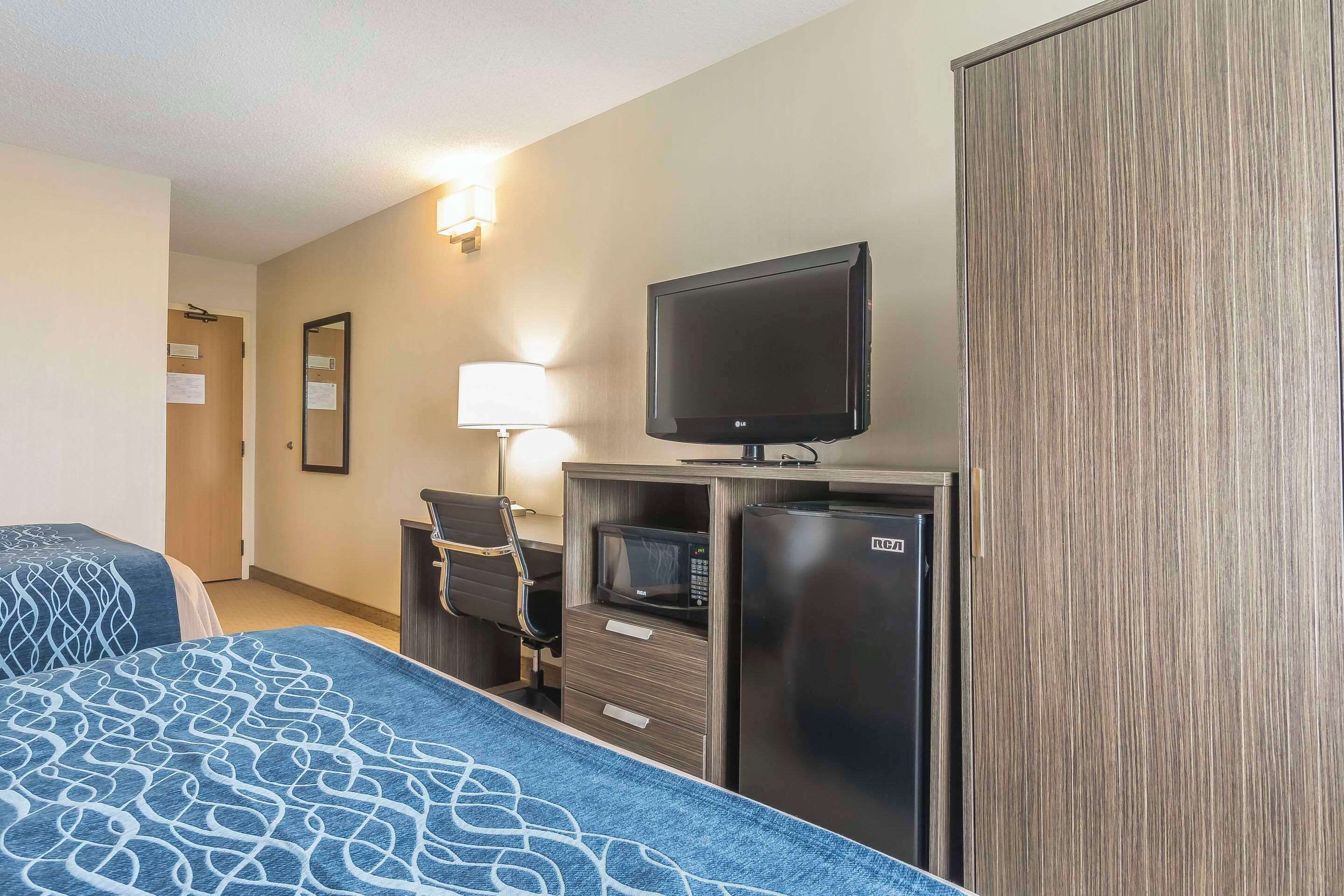 Habitación de hotel con dos camas, televisión, microondas, refrigerador, escritorio con silla y armario.