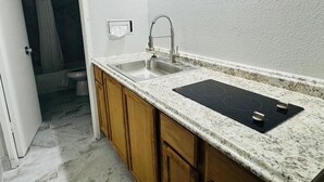 A kitchen with a double sink, wooden cabinets, a black stovetop, and a white textured wall. - Alamo Inn & Suites (Gillette)