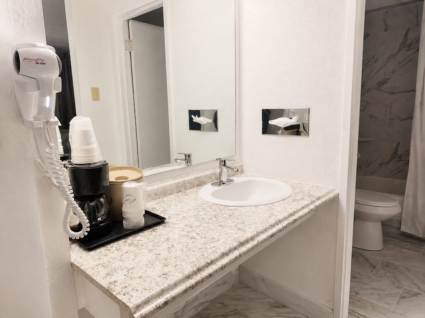 Un baño con lavamanos blanco, un espejo, un secador de pelo y un inodoro.
