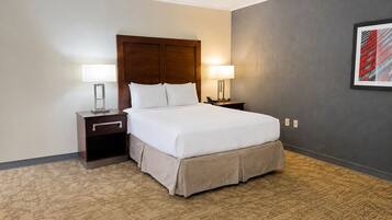 Quarto de hotel com uma cama grande, duas mesas de cabeceira com abajures, uma parede escura e um quadro emoldurado.