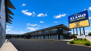 A motel with a signboard advertising Alamo Inn & Suites, featuring a modern building with a flat roof, a parking lot, and a clear blue sky. - Alamo Inn & Suites (Gillette)