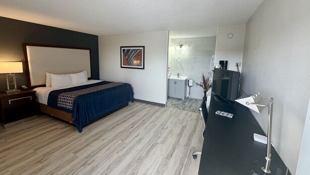 A hotel room with a bed, a desk with a lamp, a TV, and a bathroom visible through an open door. - Alamo Inn & Suites (Gillette)