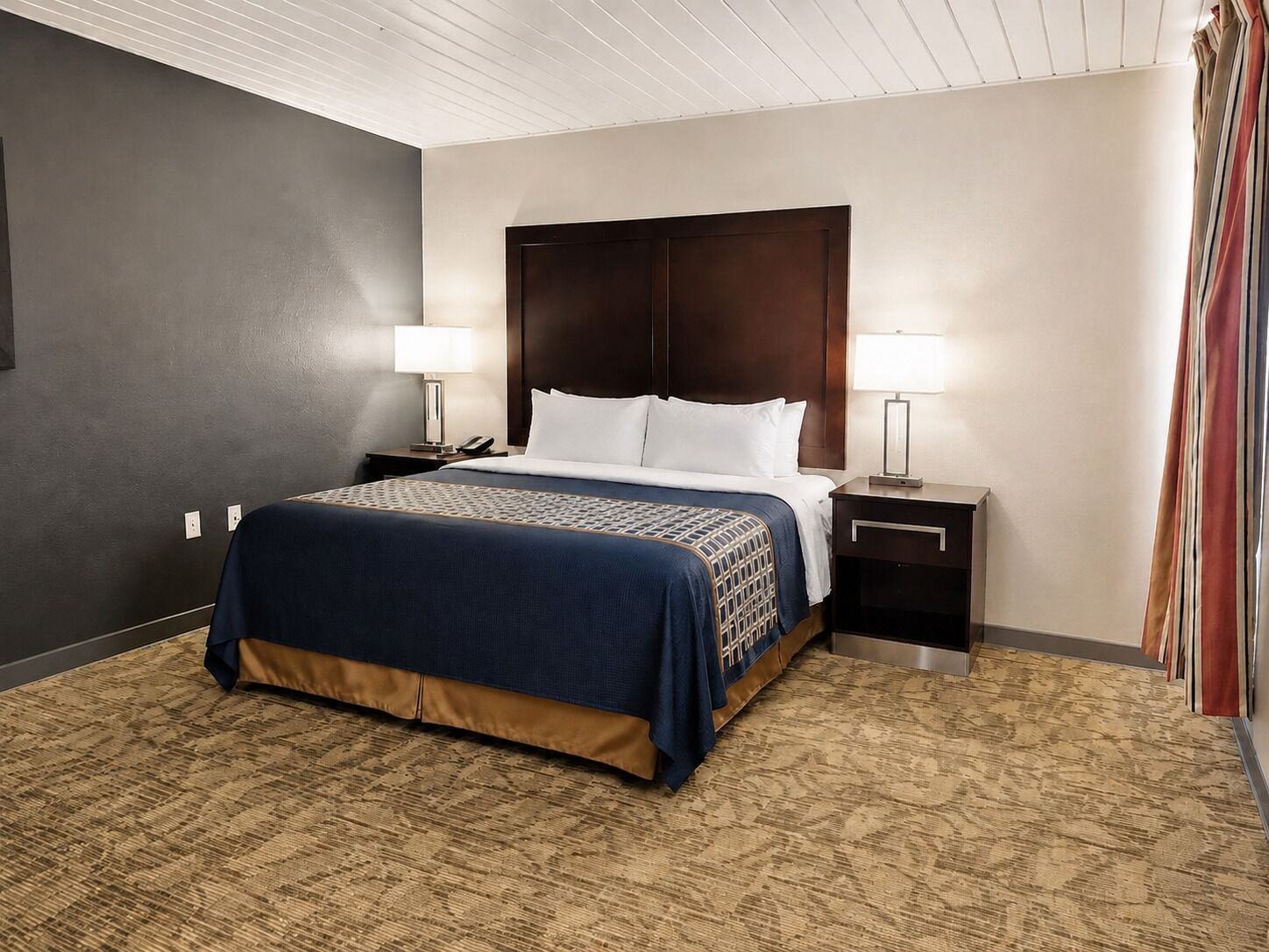 A hotel room with a large bed, two bedside tables, a headboard, and a carpeted floor.