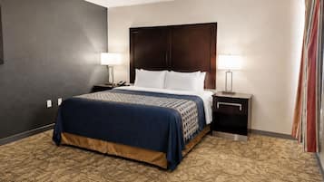 A hotel room with a large bed, two bedside tables, a headboard, and a carpeted floor.