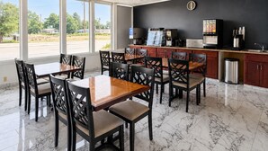 A restaurant with a marble floor, wooden tables and chairs, a coffee machine, and a view of the street. - Alamo Inn & Suites (Gillette)