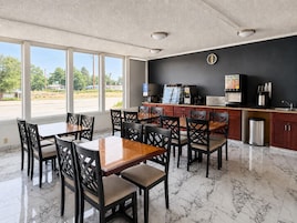 A restaurant with a marble floor, wooden tables and chairs, a coffee machine, and a view of the street.