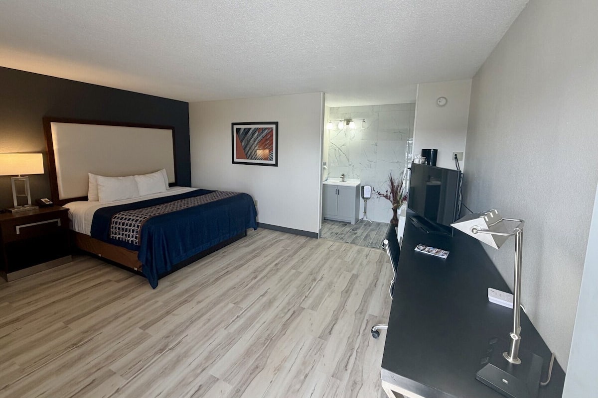 A hotel room with a bed, a desk, a TV, and a bathroom visible through an open door.