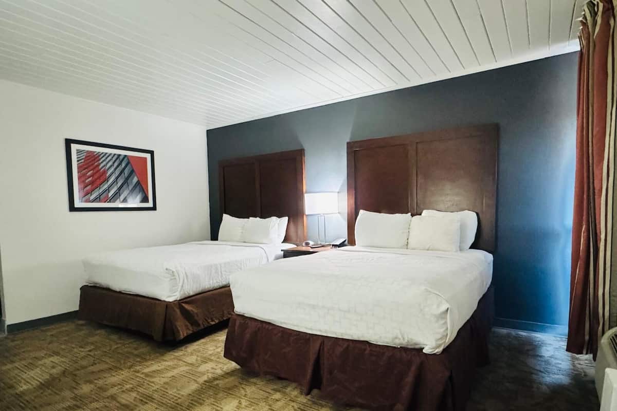 A hotel room with two beds, a nightstand, a lamp, and a framed picture on the wall.