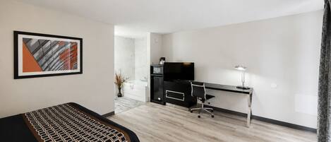 A hotel room with a bed, a desk, a television, and a bathroom visible through an open door.
