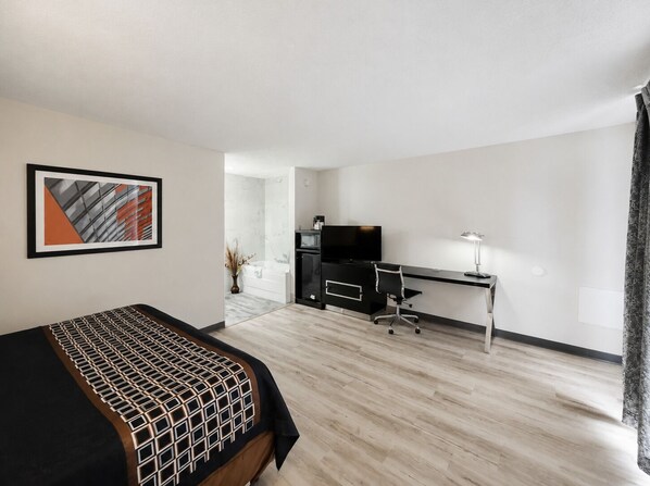 A hotel room with a bed, a desk, a television, and a bathroom visible through an open door.