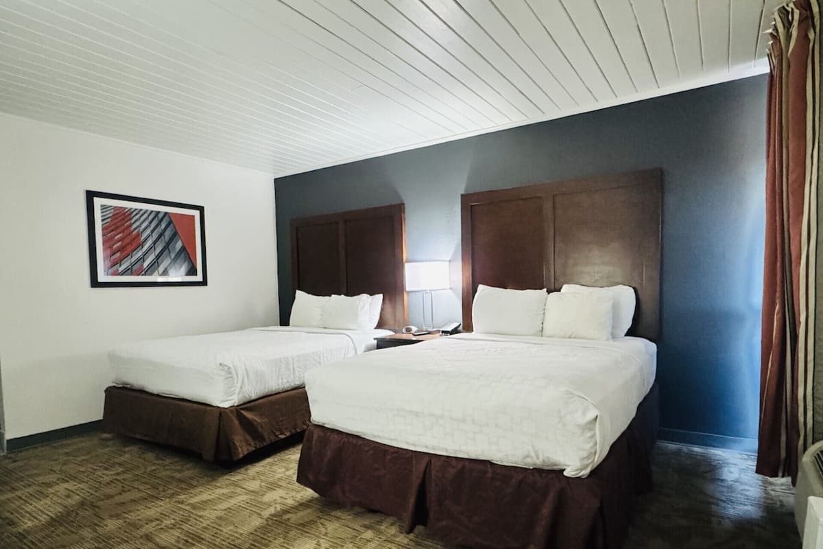 A hotel room with two beds, a wooden headboard, a framed picture on the wall, and a carpeted floor.