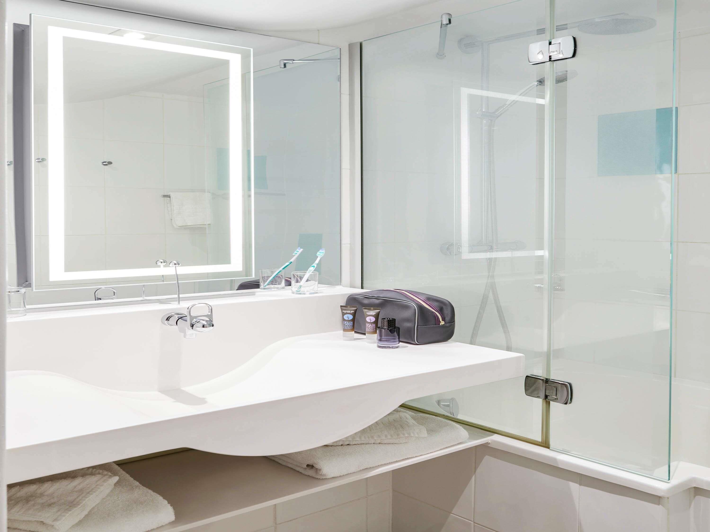 A modern bathroom with a white sink, a large mirror, and a glass shower enclosure.