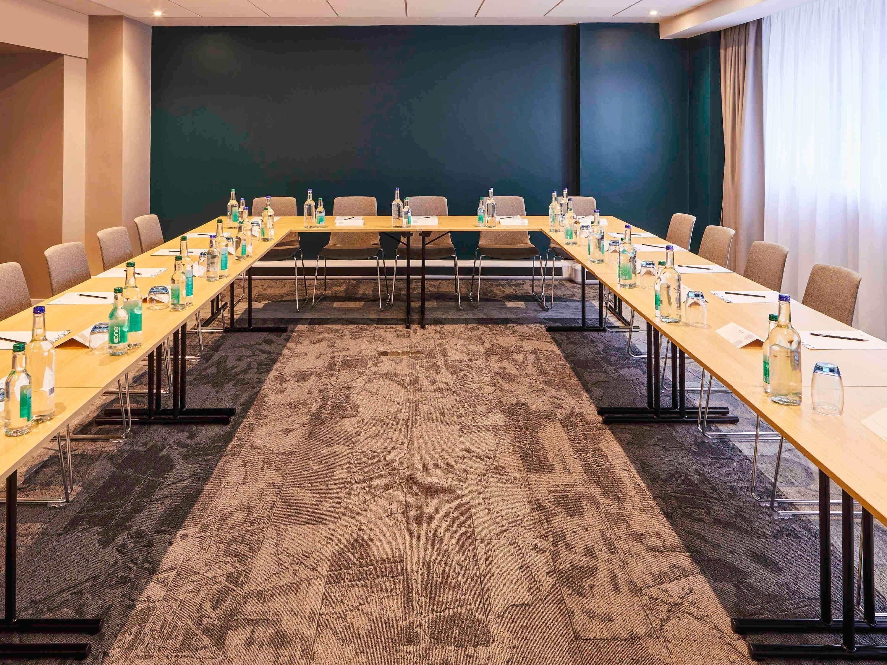 A conference room with a long table, chairs, water bottles, and a carpeted floor.