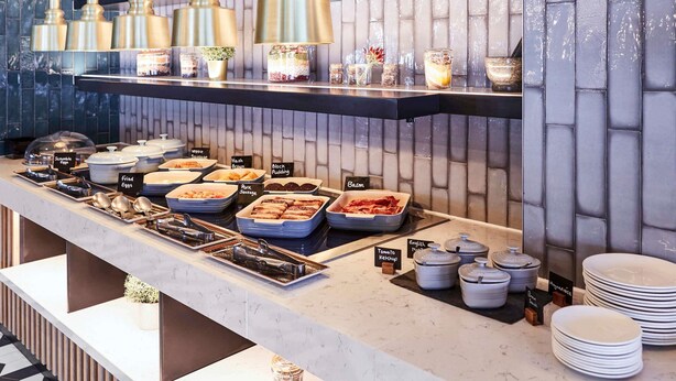 Ein Buffet mit beschrifteten Speisen, einer Marmorplatte und hängenden Pendelleuchten.