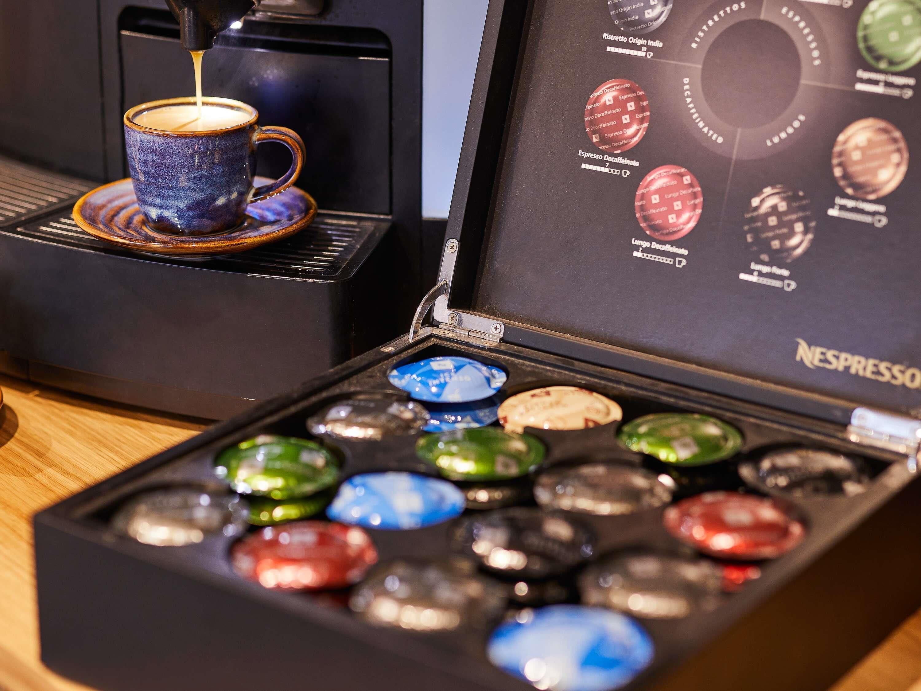 A coffee machine with a cup of coffee, a menu board, and a box of coffee capsules.