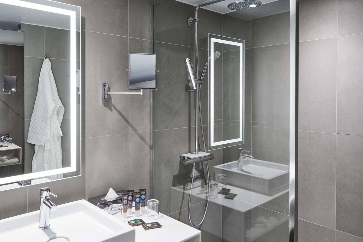 A modern bathroom with a glass-enclosed shower, a large mirror, and a vanity with a sink and toiletries.