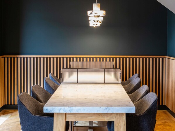 A dining area with a rectangular table, cushioned chairs, and a hanging light fixture.