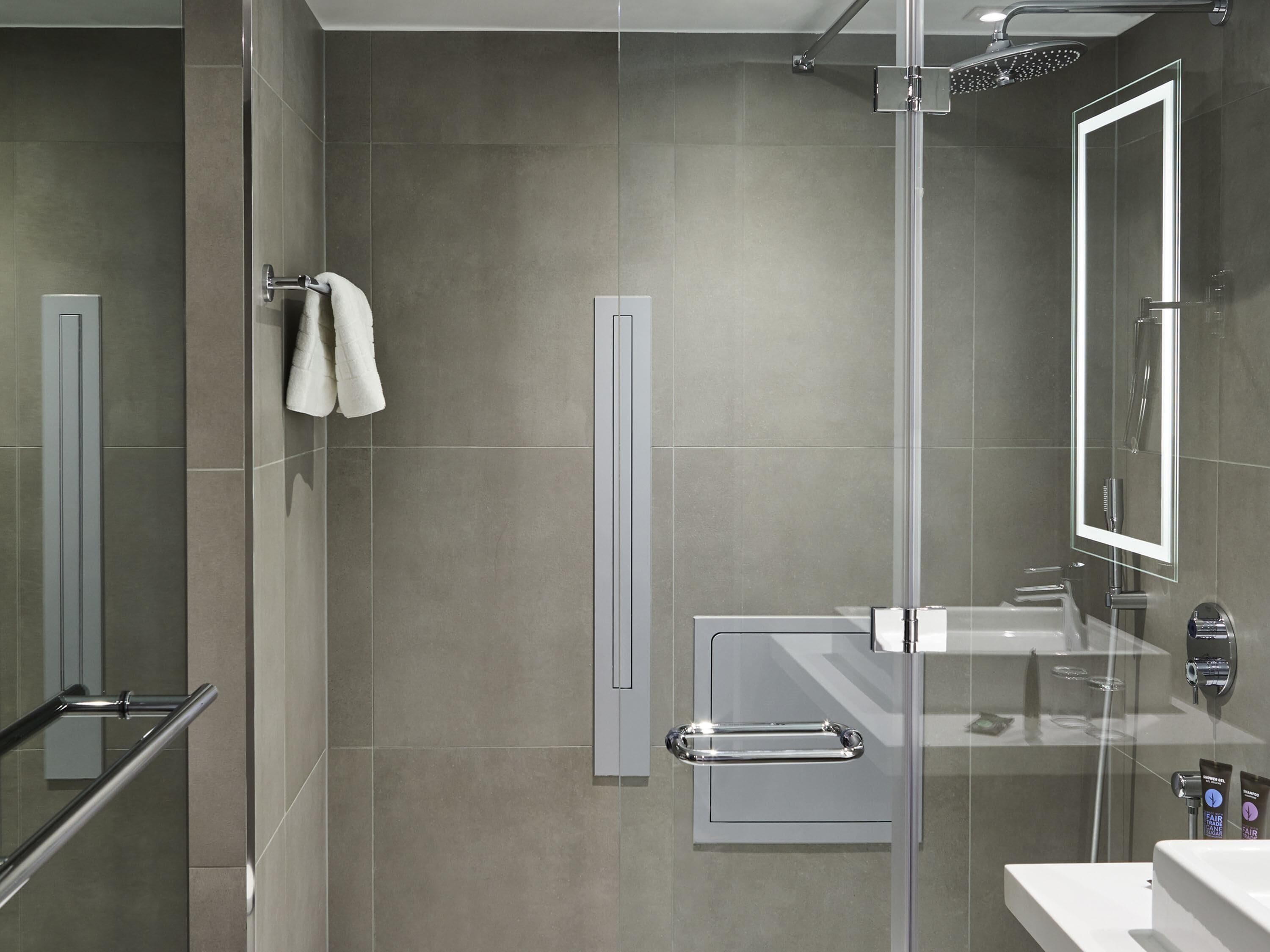 A modern bathroom with a glass shower enclosure, a towel rack, a glass door, and a vanity with a mirror.