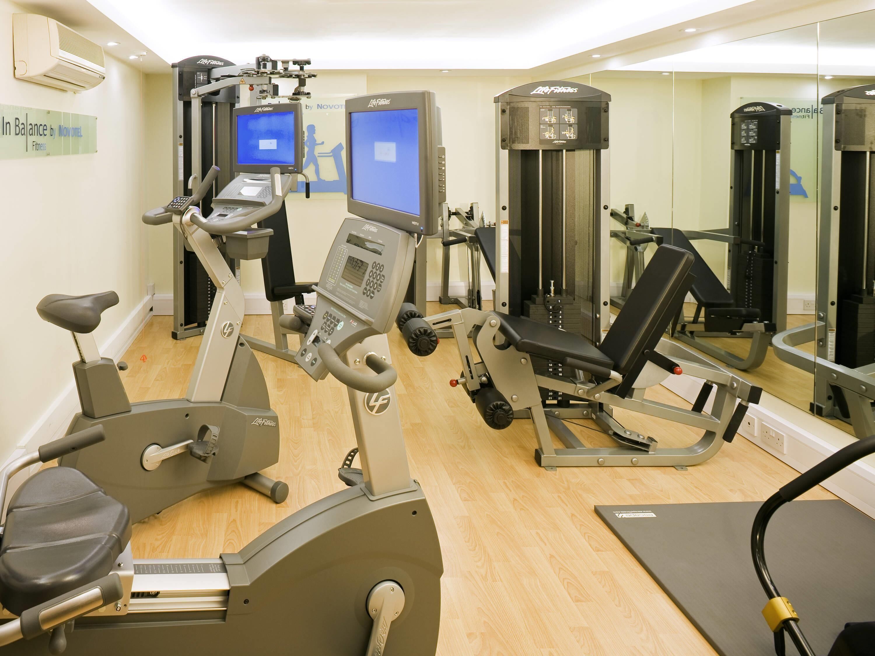 Un gimnasio con equipo de cardio, máquinas de pesas y un espejo grande.