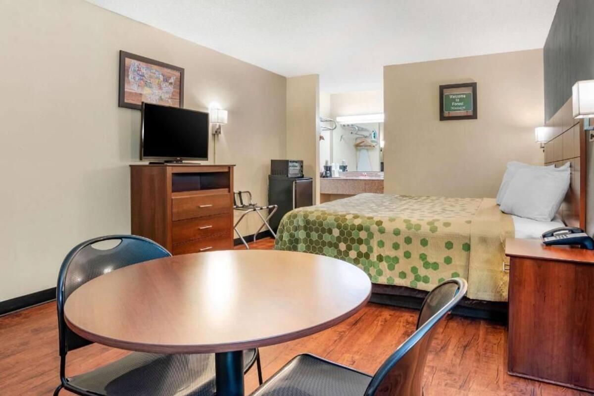A hotel room with a bed, a desk, a chair, a television, a dresser, and a mirror.