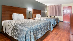 A hotel room with two beds, a wooden headboard, a desk, a chair, and a red door.