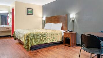 A hotel room with a bed, bedside table, chair, and a wall-mounted lamp.