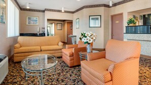 A hotel lobby with a patterned carpet, orange armchairs, a glass coffee table, and a sofa.