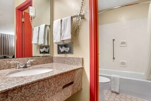 A bathroom with a granite countertop sink, a mirror, and a shower area.