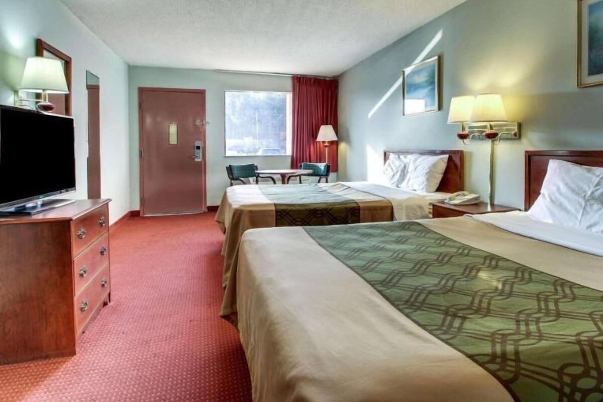 A hotel room with two beds, a desk, a television, and a window with curtains.