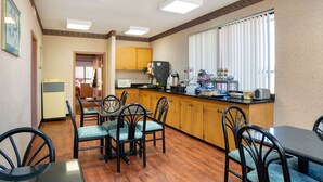 A compact kitchen with wooden cabinets, a black countertop, and a dining area with four chairs and a table.
